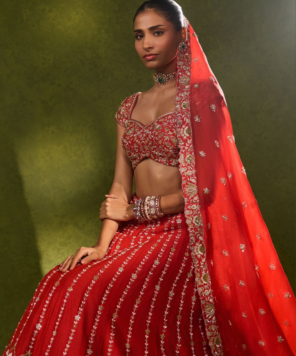 ANANDI LEHENGA - Red raw silk lehenga meticulously crafted with intricate resham, zardozi, pearl and glass beadwork paired with a zardozi-embellished floral work cap sleeve blouse -  Leher by Chamee and Palak