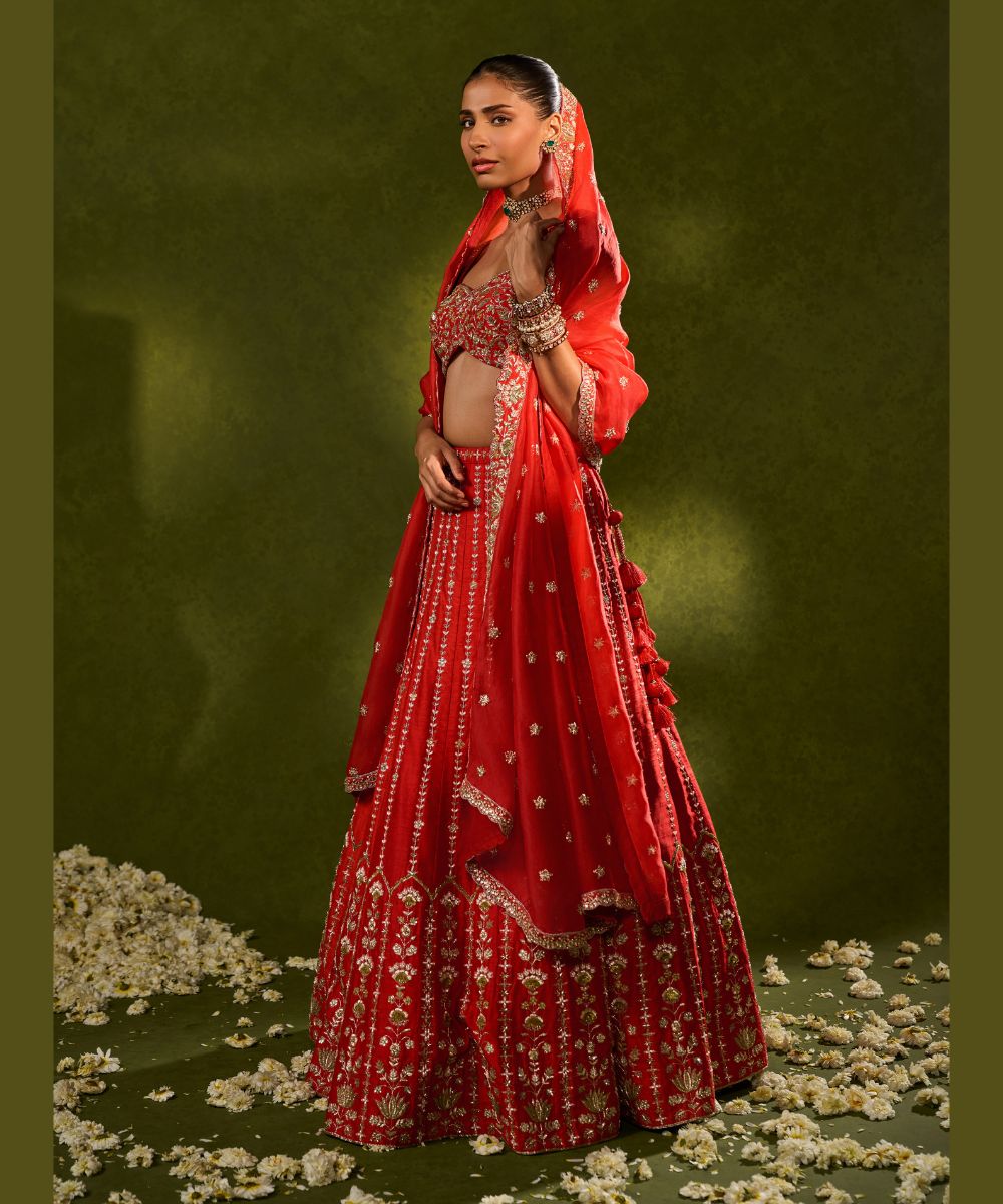 ANANDI LEHENGA - Red raw silk lehenga meticulously crafted with intricate resham, zardozi, pearl and glass beadwork paired with a zardozi-embellished floral work cap sleeve blouse -  Leher by Chamee and Palak